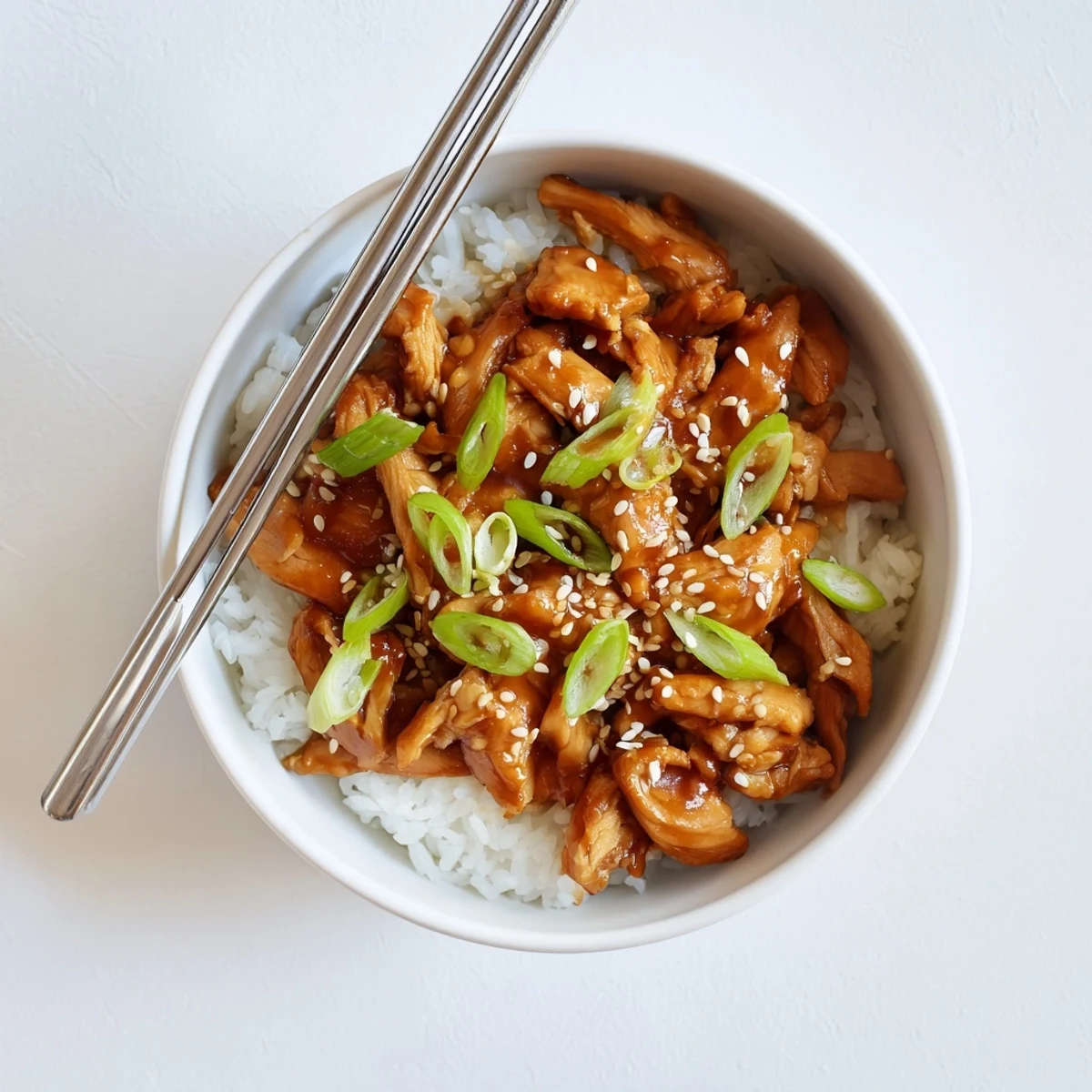 Garnished bowl of Crockpot Teriyaki Chicken over white rice with green onions and sesame seeds