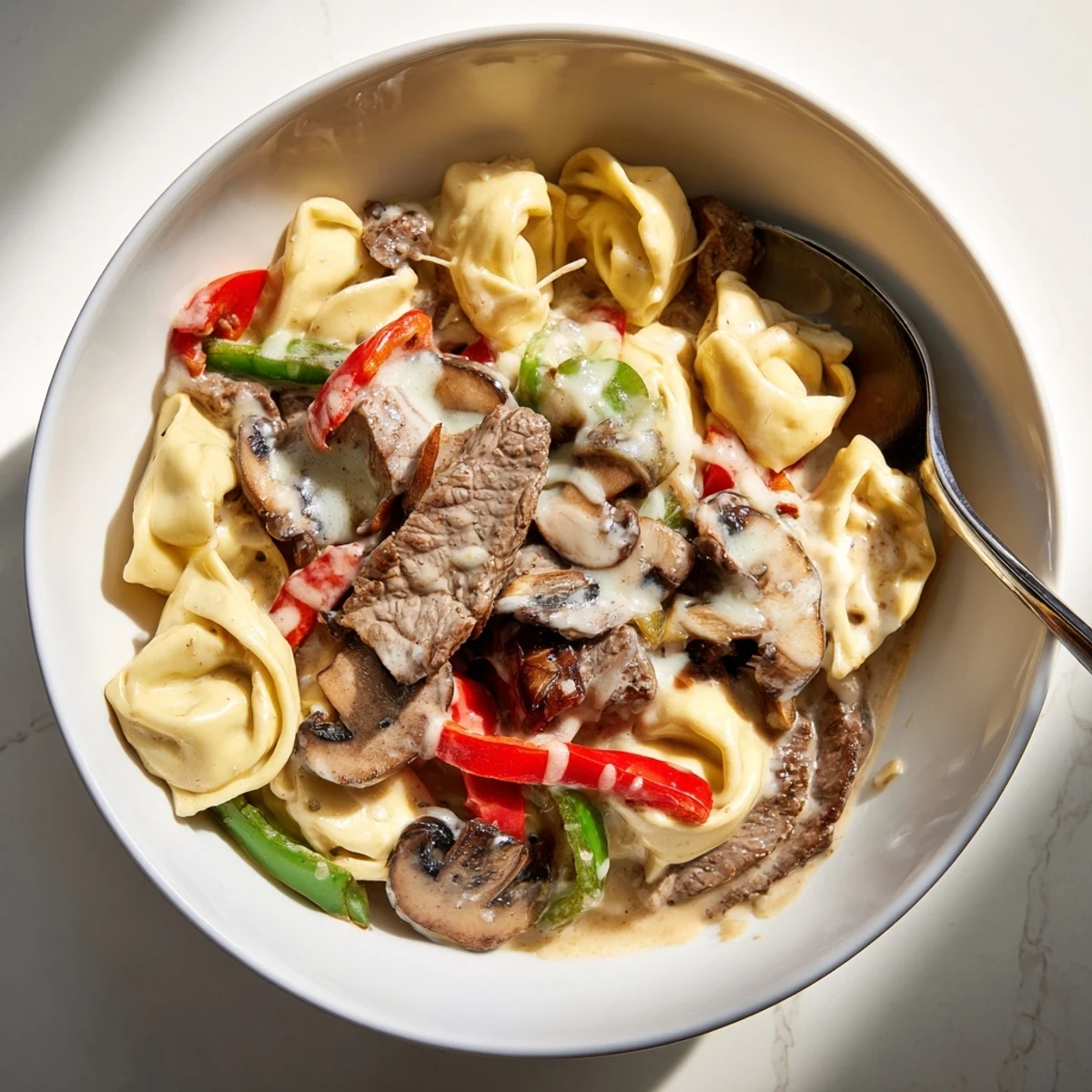 Hearty crock pot cheesesteak tortellini bowl featuring seared beef, vegetables, and three cheeses over tender tortellini