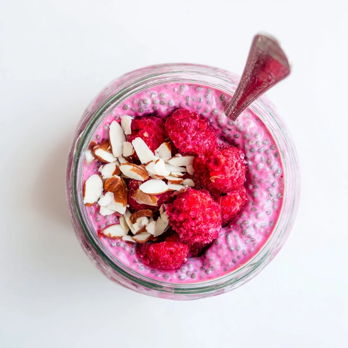 Creamy raspberry chia pudding topped with fresh berries and mint in glass jars