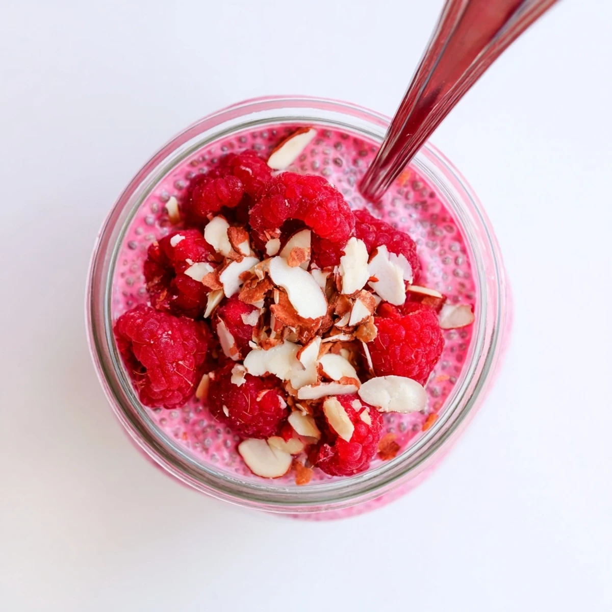 Thick pink raspberry chia pudding bowl garnished with granola and whole raspberries