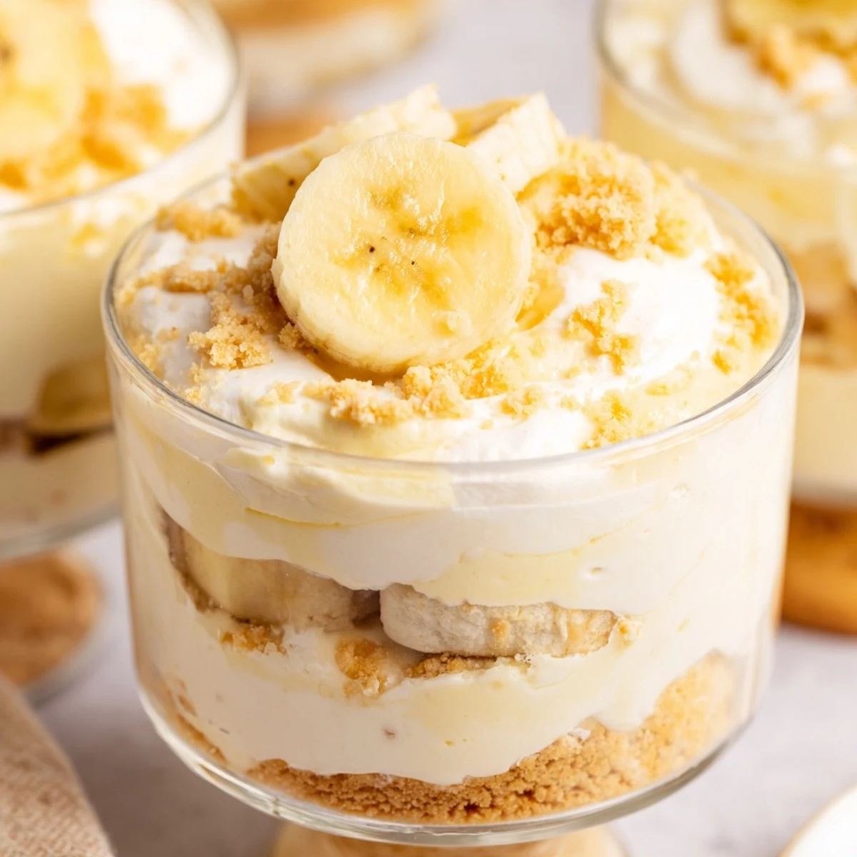 Individual no bake banana pudding cheesecake cups featuring layered pudding, cheesecake filling, and crunchy cookie topping