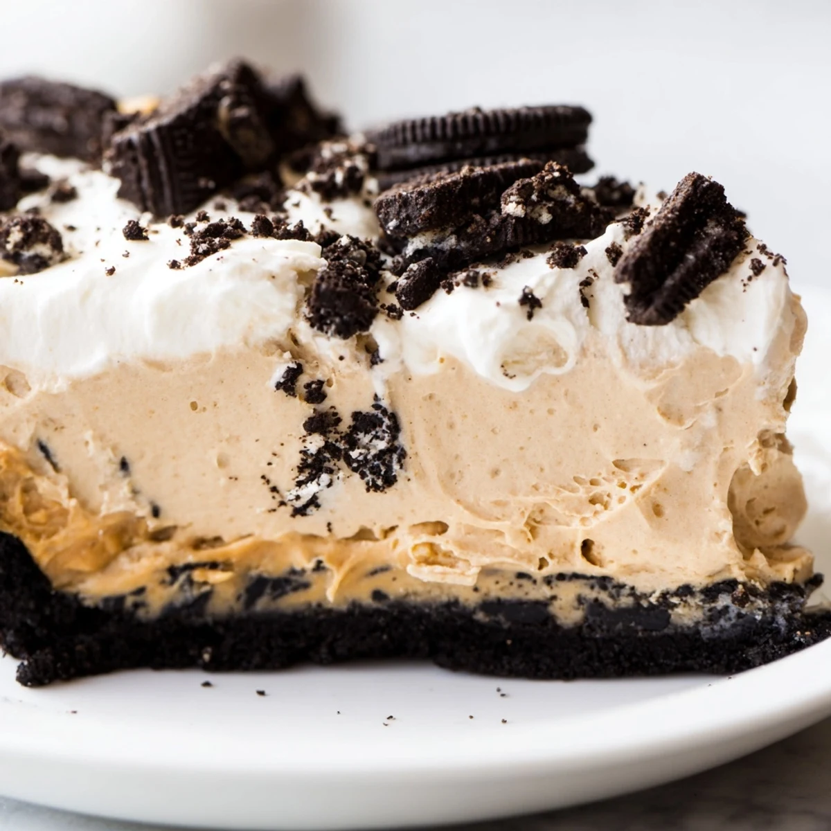 Creamy peanut butter Oreo pie sliced thick with fluffy whipped cream and cookie crumbles