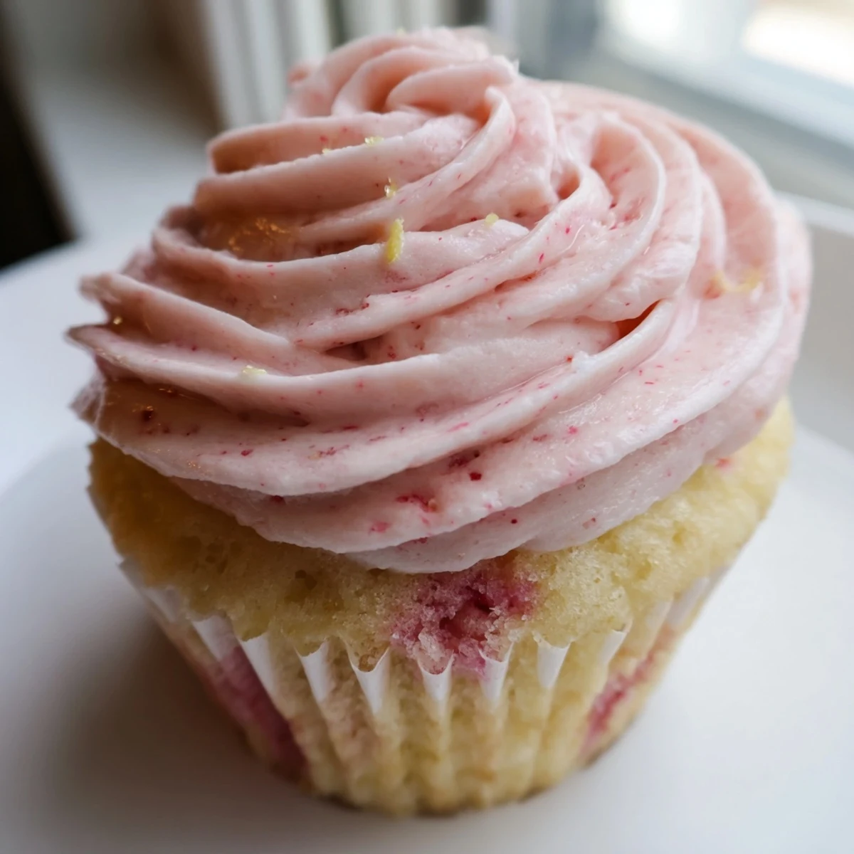 Strawberry lemonade cupcakes with pink buttercream frosting on rustic white cake stand