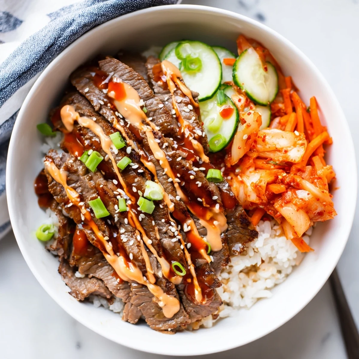 Korean BBQ steak rice bowls topped with crisp veggies, kimchi, and creamy Sriracha drizzle