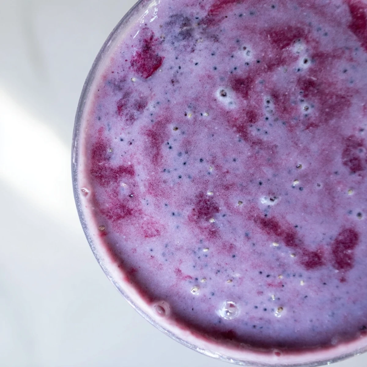 Thick purple chia seed smoothie topped with fresh berries and chia seed garnish in glass