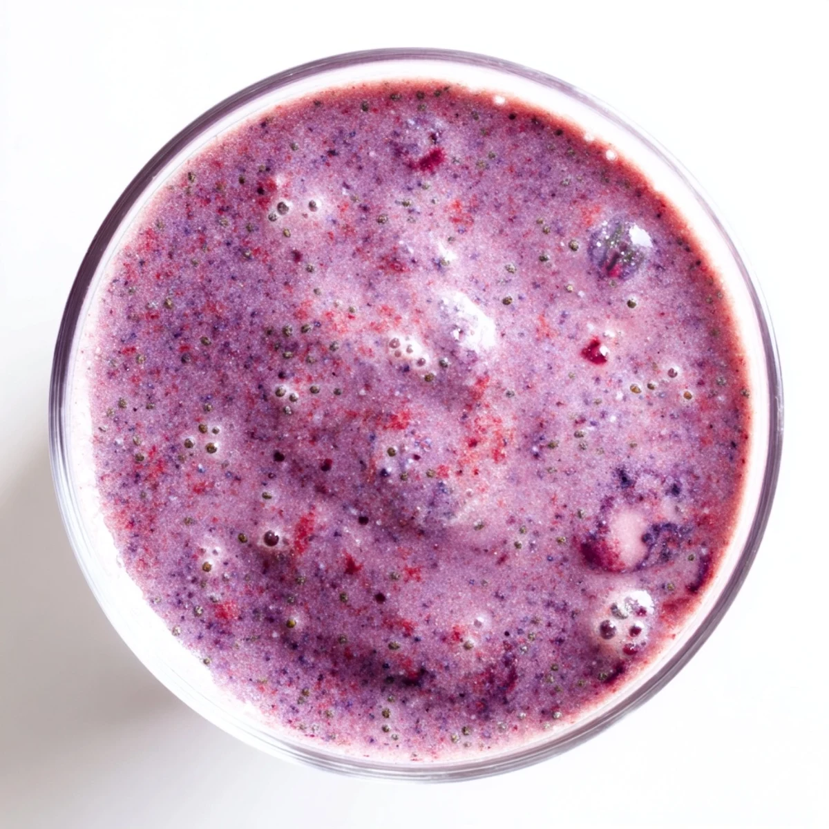 Vibrant purple chia seed smoothie with floating seeds and sliced strawberry on glass rim