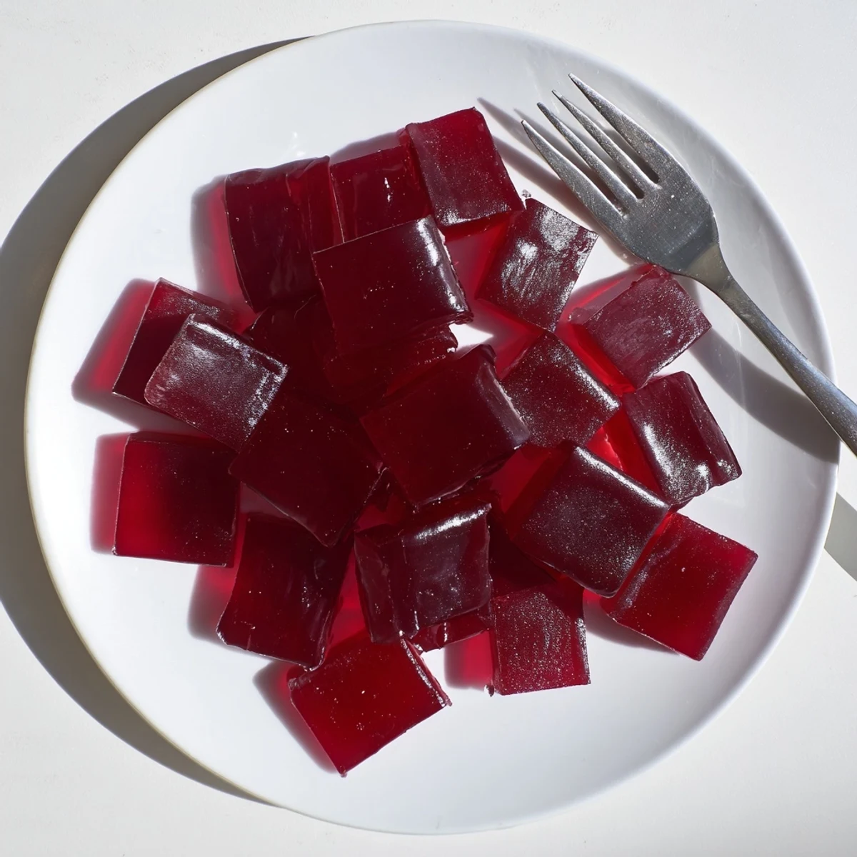 Chewy homemade raspberry gummy snacks arranged in a neat row on a white plate